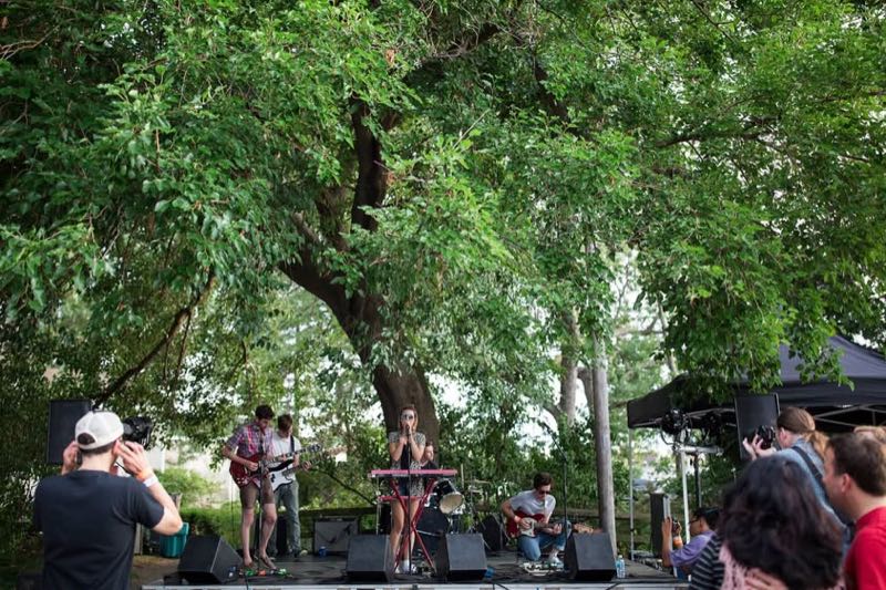 Festivalgoers watch a band on a stage beneath the trees at Dunham Tavern.