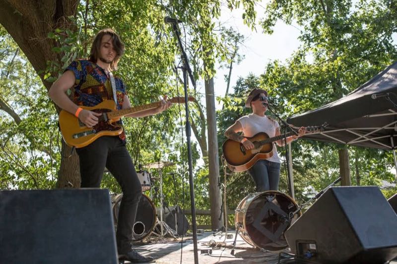 A guitarist in a patterned shirt plays beside an acoustic guitarist.