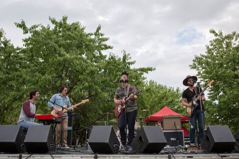 A five-piece band plays in front of the trees as evening falls.