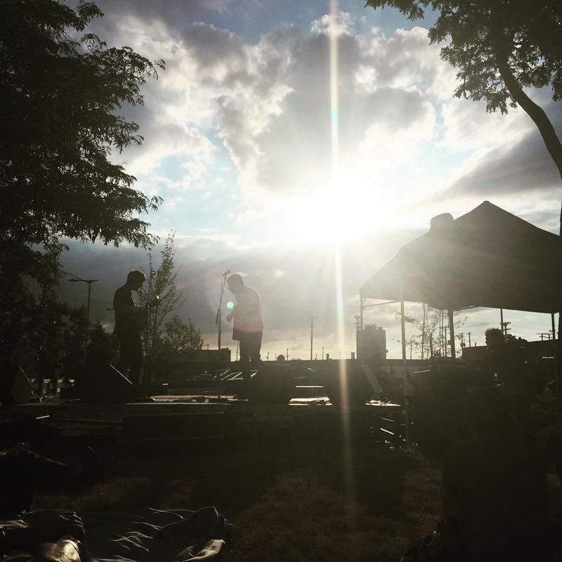 The sun sets behind a stage and tents in the garden.