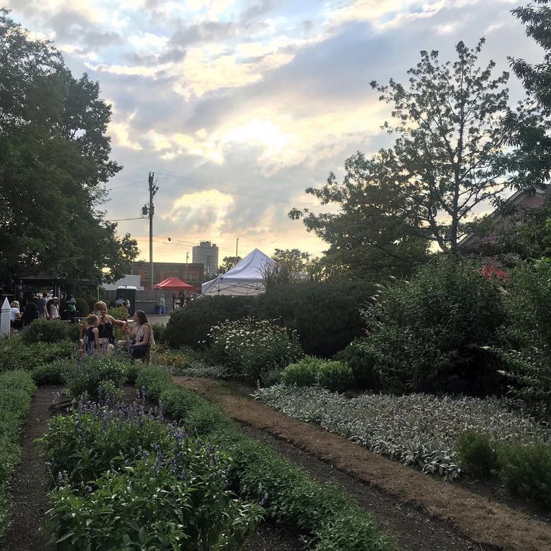 Garden paths and plantings at Dunham Tavern, with festival tents beyond.